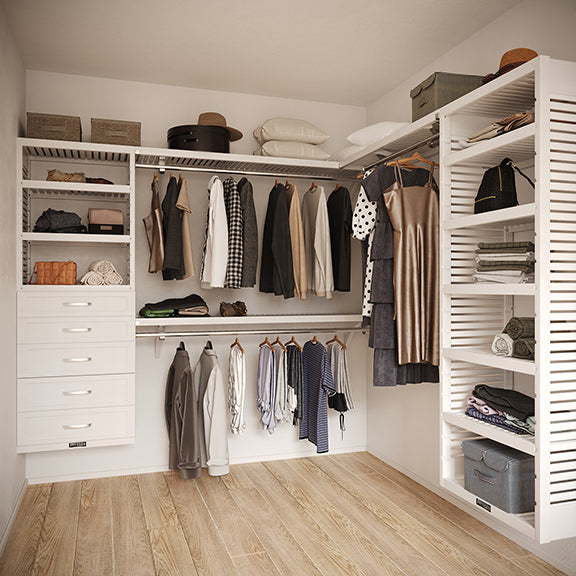 White L Shaped walk in closet organizer with 5 drawers,  clothes and hanging in a room.