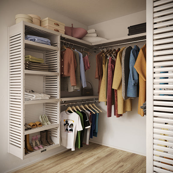 White U shaped walk in closet organizer with wooden shelves, hanging clothes, and shoes on a wooden floor.