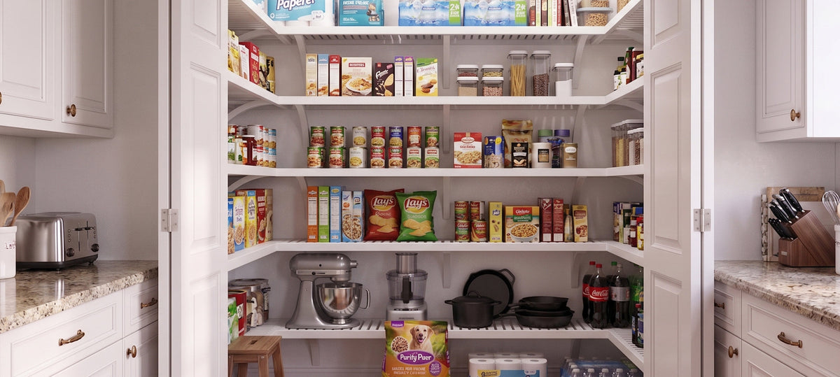 A well-organized white pantry with open shelving stocked with various food items, canned goods, kitchen appliances, and storage containers, framed by white cabinets and granite countertops.