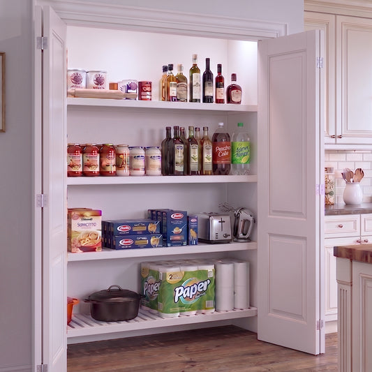An open reach-in pantry with white finished wood shelves stocked with food items within a white kitchen interior.