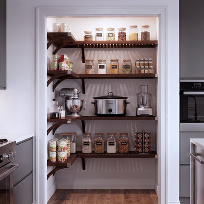 A small L shaped walk-in pantry with four levels of espresso solid wood shelving filled with grocery items.