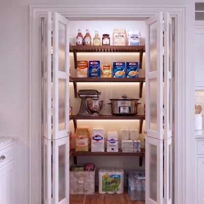 A small U shaped walk-in pantry with four levels of chestnut solid wood shelving filled with grocery items.