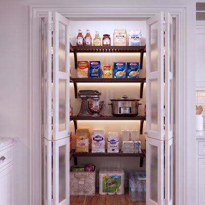 A small U shaped walk-in pantry with four levels of espresso solid wood shelving filled with grocery items.