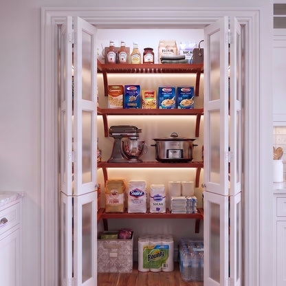 A small U shaped walk-in pantry with four levels of red mahogany solid wood shelving filled with grocery items.
