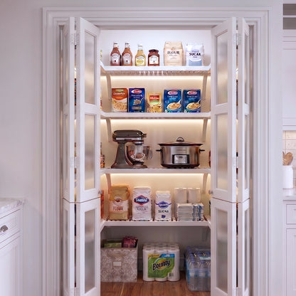 A small U shaped walk-in pantry with four levels of white solid wood shelving filled with grocery items.