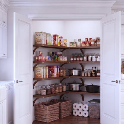 A fully stocked L shaped walk-in pantry with 4 tiers of chestnut solid wood shelves filled with kitchen appliances and grocery foods.