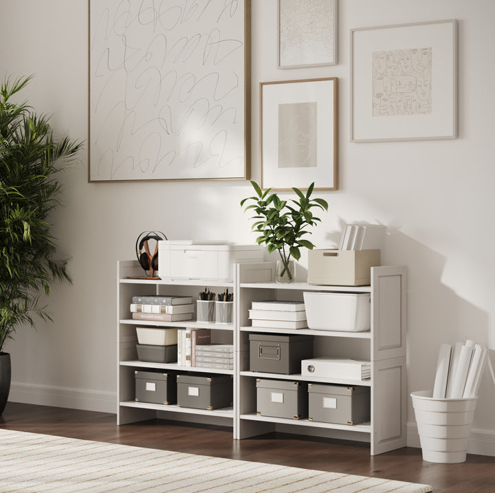 White storage shelves with boxes and bins in a room with framed art on the wall.